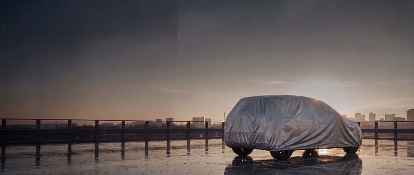 Silver cover on a hatchback on a wet rooftop car park after rain at dusk