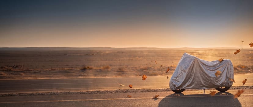 Silver cover on a cruiser motorcycle beside a desert highway with leaves blowing past in the late sun