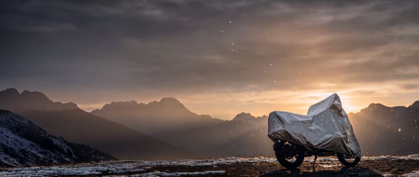 Silver cover on an adventure motorcycle dusted with snow on a mountain ridge at sunset