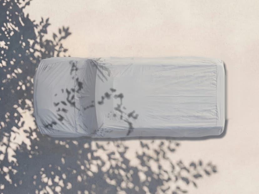 Top-down view of a light grey cover fitted over a Hummer on pale pavement with tree shade.