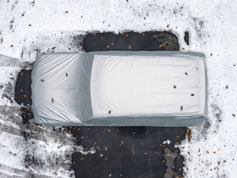Top-down view of a silver reflective cover fitted over a Hummer on snowy ground with a few fallen leaves.