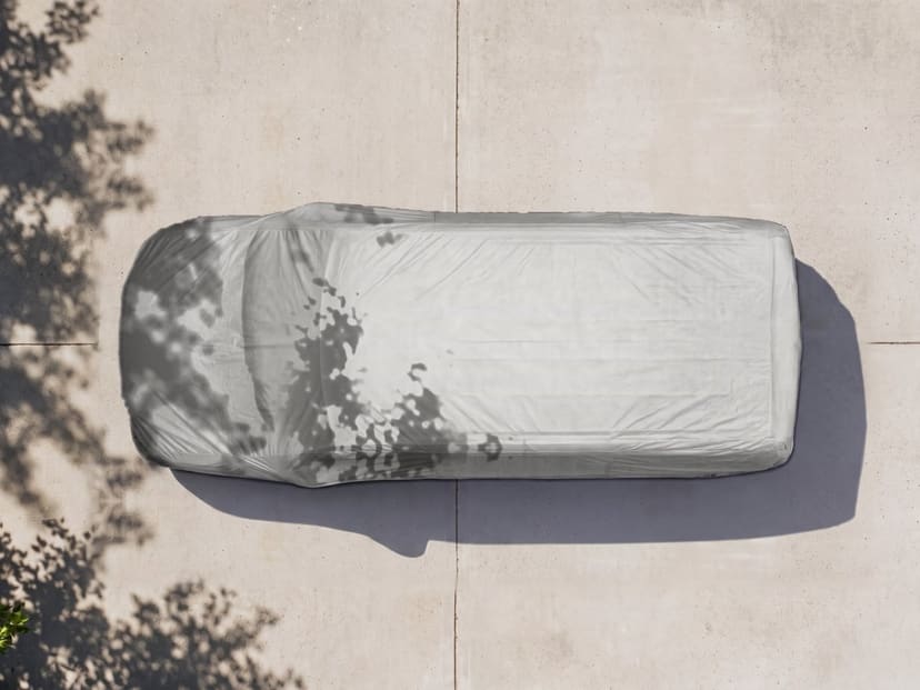 Top-down view of a light grey cover fitted over a minivan on pale pavement with tree shade.