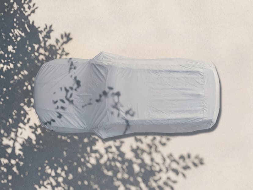 Top-down view of a light grey cover fitted over an SUV on pale pavement with tree shade across the ground.