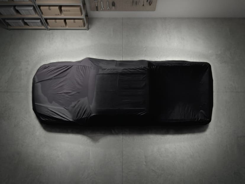 Top-down view of a black stretch cover fitted over a pickup truck on a concrete garage floor.