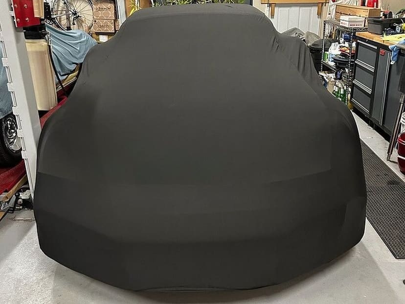 The same Porsche 911 Turbo under a black Satin Protect cover in the same garage, seen from the front