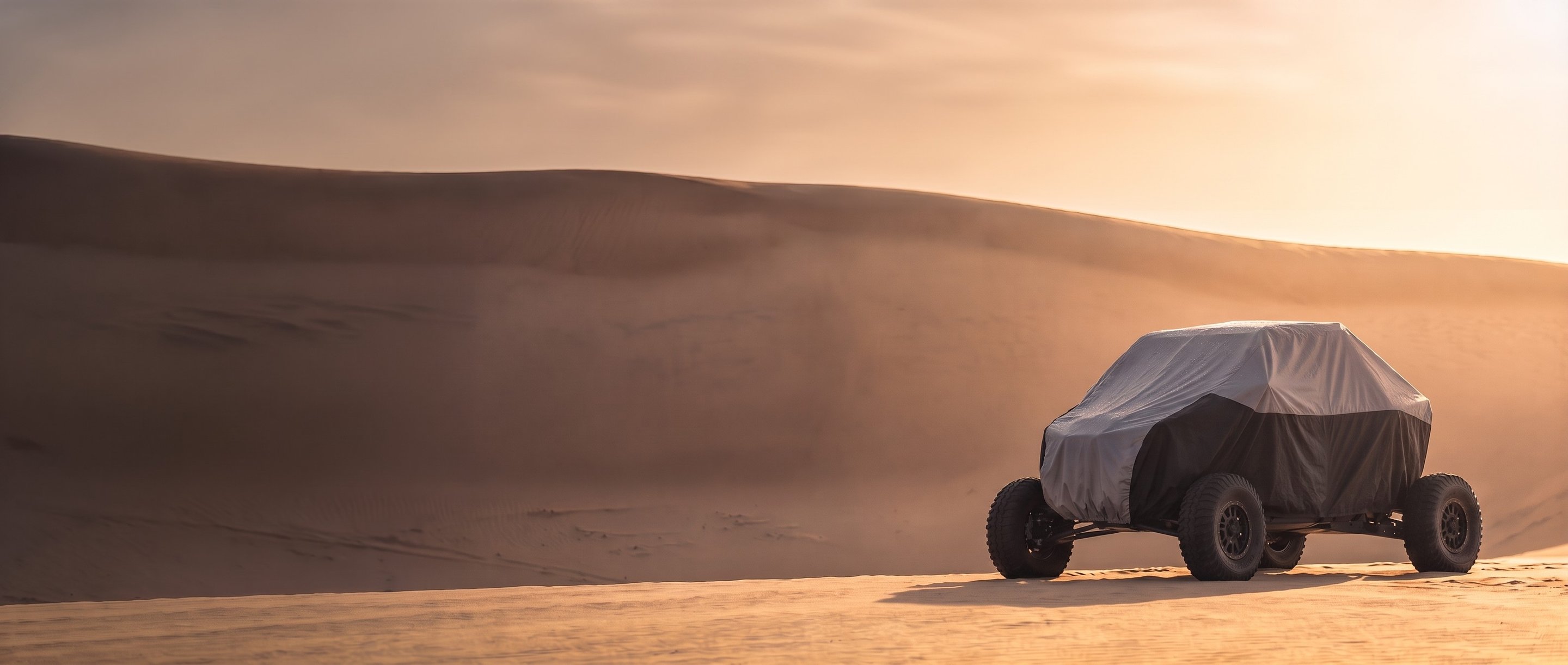 Two-tone cover on a sport side-by-side parked on calm sand dunes in low sun